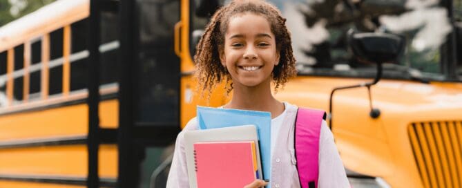 young student with books standing in front of school bus