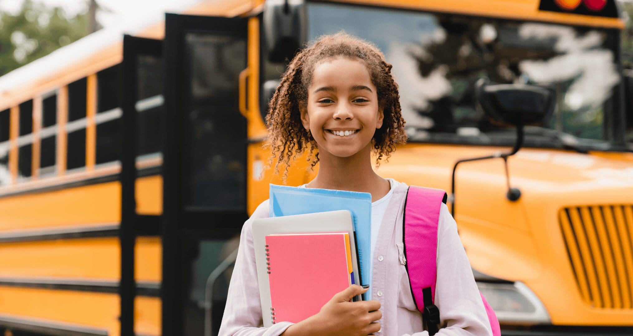 young student with books standing in front of school bus