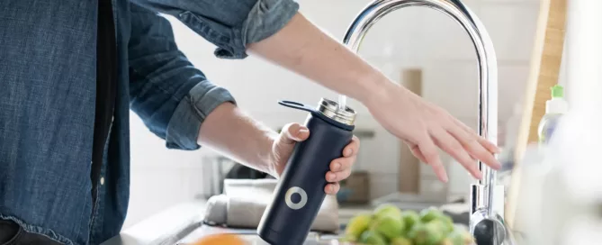 woman filling water bottle from sink