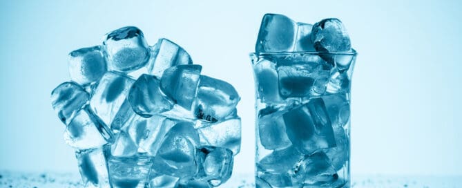 melting ice cubes near glass and in glass, on white with drops