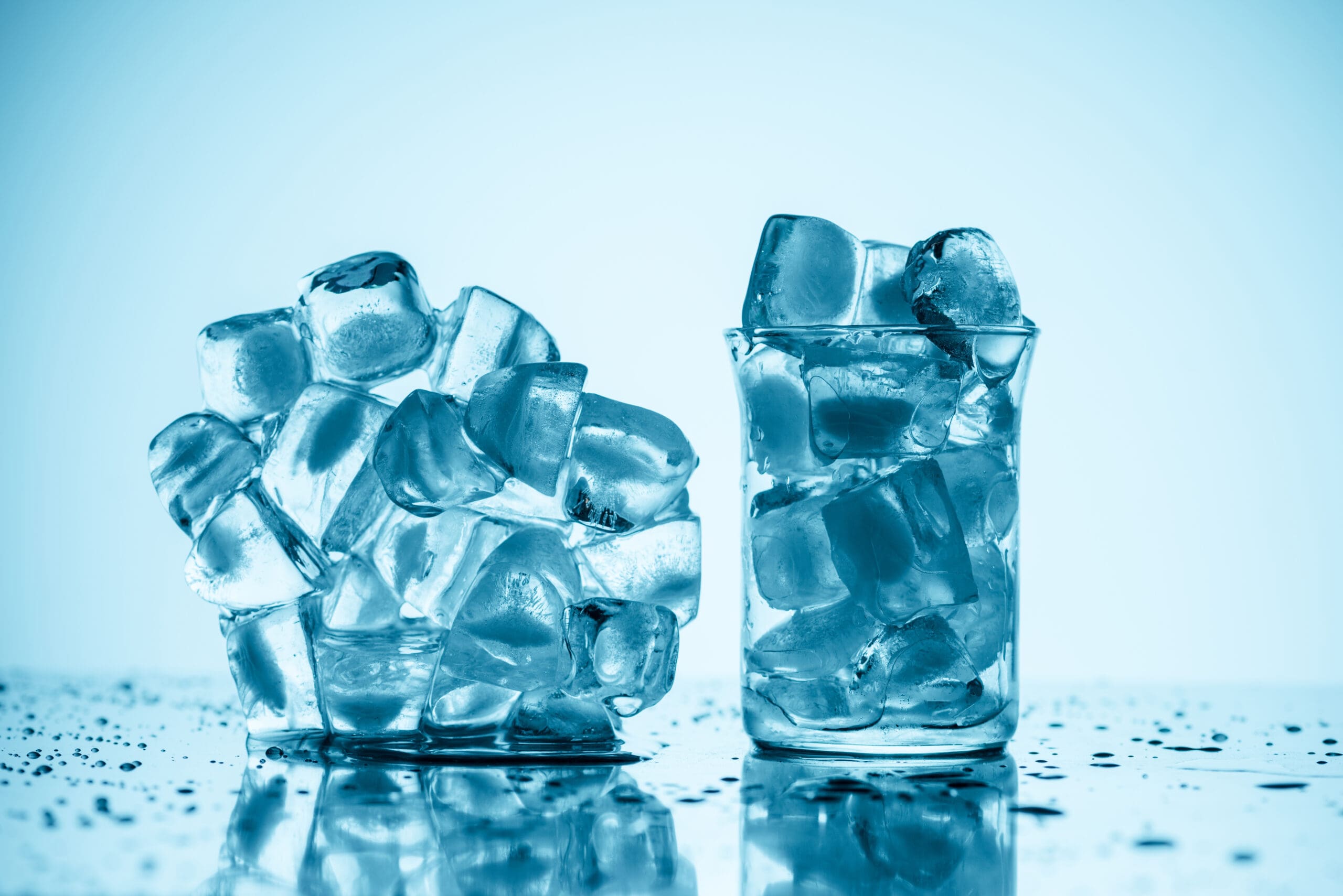 melting ice cubes near glass and in glass, on white with drops