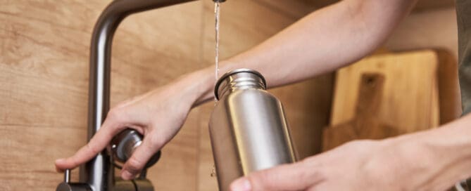 woman filling up reusable water bottle with tap water