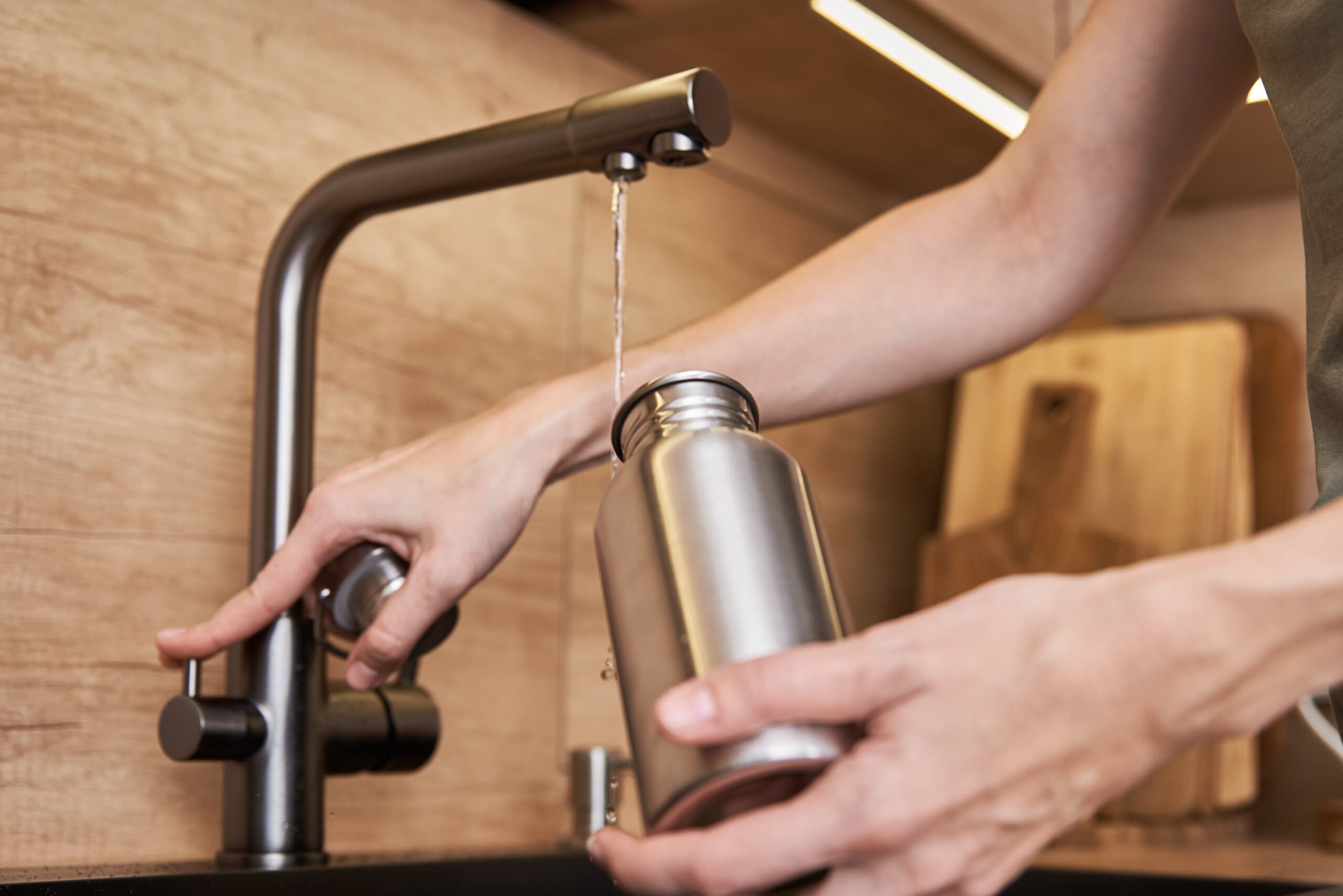 woman filling up reusable water bottle with tap water