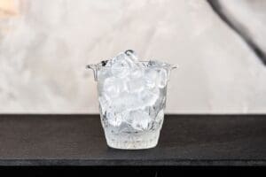 Ice bucket filled with cubes of ice sitting on a black textured table Ice bucket with ice cubes