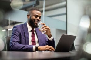 Positive black manager drinking water while working on laptop african amercian manager drinking water while working on laptop