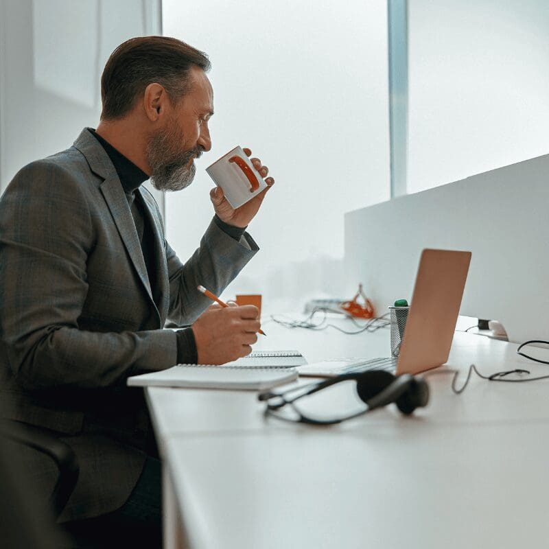 businessman-holding-cup-while-writing-in-the-office businessman drinking from a cup at his desk